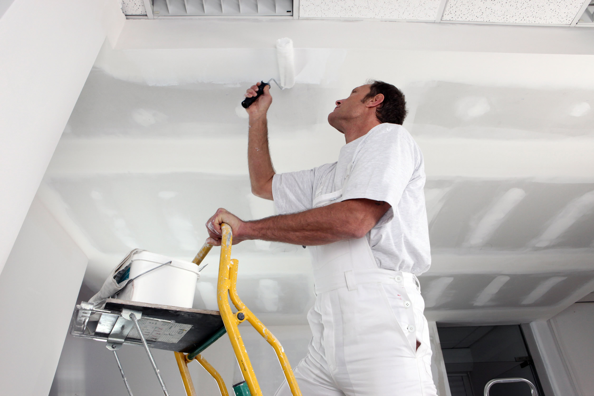 Profesional vertiendo pintura blanca en la bandeja antes de pintar una habitación